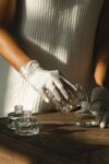 Unrecognizable crop African American female pouring essential oil in glass bottle while making liquid incense at table